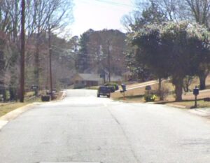typical suburban Atlanta neighborhood with single-story houses and tall trees. A black SUV is parked on the right side. Width is about 20 meters and notice the use of speed tables to get people to slow down. 